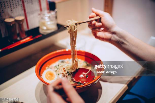 cropped hand of woman eating a bowl of freshly served traditional japanese ramen with chopsticks in a japanese restaurant. asian cuisine and food culture. eating out lifestyle - noodle stock pictures, royalty-free photos & images