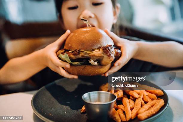 close up shot of lovely little asian girl enjoying eating a big burger with sweet potato fries in a restaurant. eating out lifestyle - kid eating burger bildbanksfoton och bilder