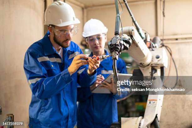 male engineer trains a female engineer for how to operate a robotic welding machine in a workshop. - maschinenbau stock-fotos und bilder