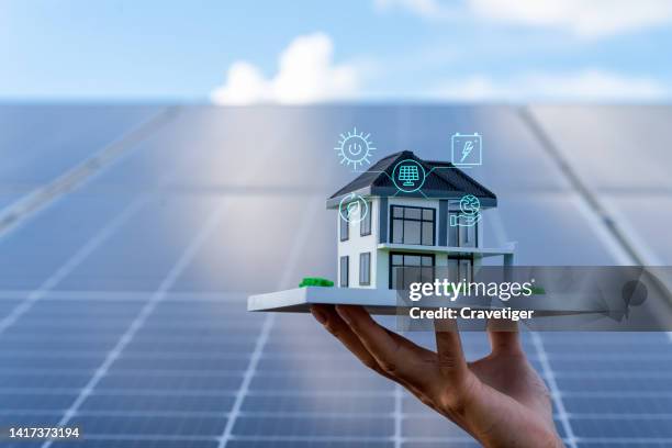 an architectural model with solar panels . concept energy saving and sustainable resource . the model of house lift by hand on the solar panel with digitization display , photovoltaic against with sun light and reflex on solar panel . - zonnepanelen stockfoto's en -beelden