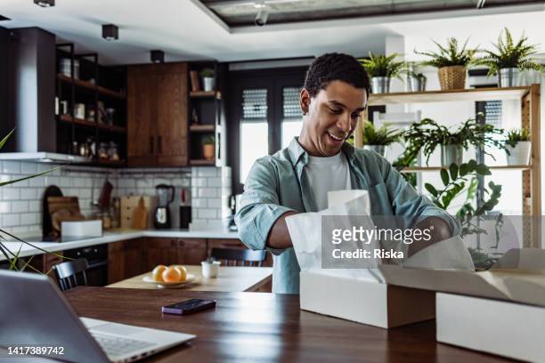 smiling young man unboxing online purchase at home - caixa aberta imagens e fotografias de stock
