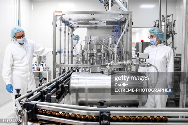 zwei voll ausgestattete mitarbeiter in schützender arbeitskleidung in einem pharmazeutischen labor - arzneimittelherstellung stock-fotos und bilder