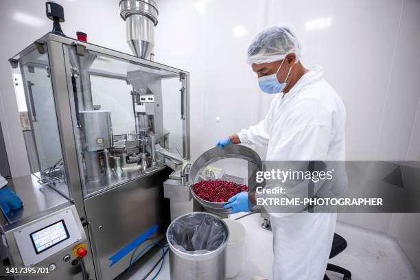 male employee seen in a laboratory while holding a big bowl with red and black pills during working in a laboratory - big pharma stockfoto's en -beelden