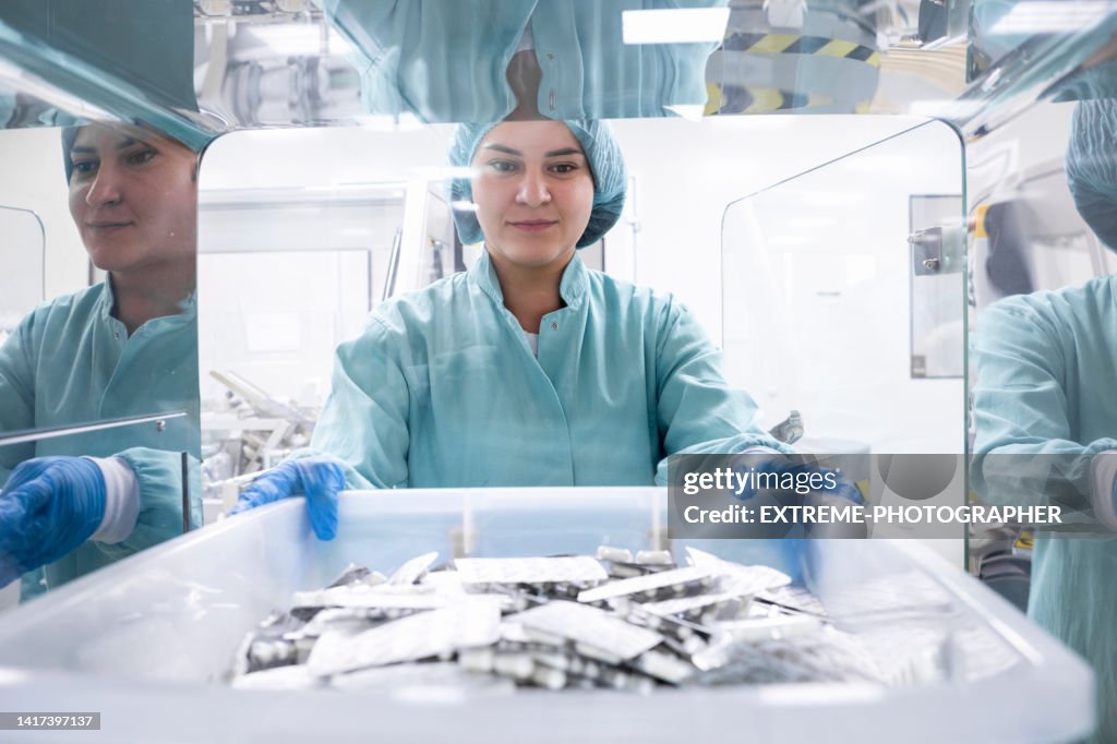 Pharmamitarbeiter in der Hand einer Schachtel mit zahlreichen Blisterpackungen in einem speziellen Raum gesehen