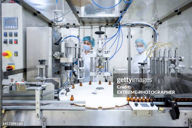 dos empleadas en un laboratorio farmacéutico vistas mientras controlan el proceso de fabricación de medicamentos - fábrica farmacéutica fotografías e imágenes de stock