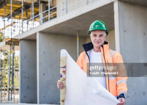 smiling senior construction worker with blueprint at site - architekt mit plan frontal stock-fotos und bilder