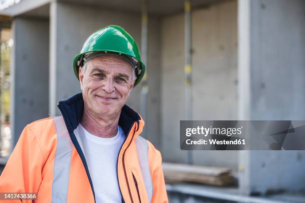 smiling building contractor standing at construction site - laborer stock-fotos und bilder