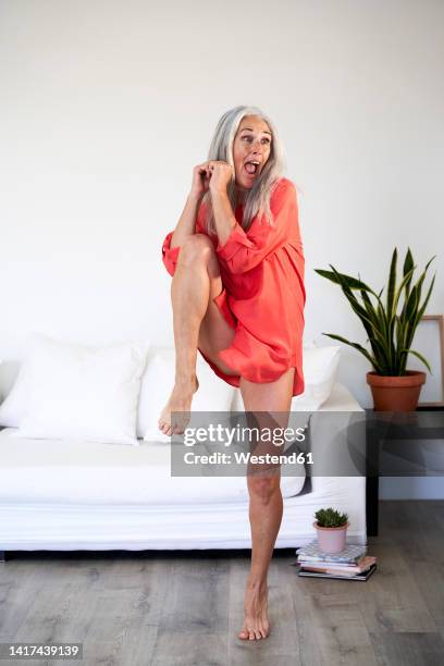 mature woman with mouth open dancing in living room at home - op een been staan stockfoto's en -beelden