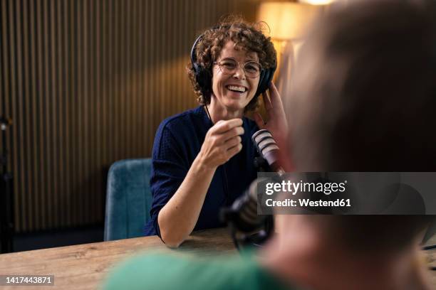 happy presenter wearing eyeglasses talking with guest in radio station - presentator media stockfoto's en -beelden