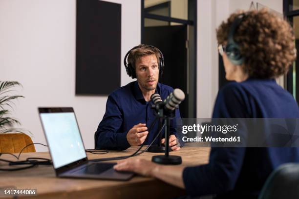 man wearing headset talking with guest in recording studio - podcasting - fotografias e filmes do acervo