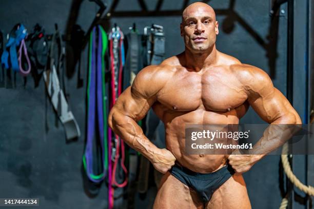 confident bodybuilder with arms akimbo flexing muscles in gym - bodybuilderin stock-fotos und bilder