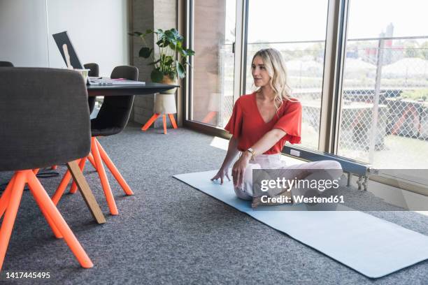 businesswoman doing yoga on exercise mat in office - blonde yoga foto e immagini stock