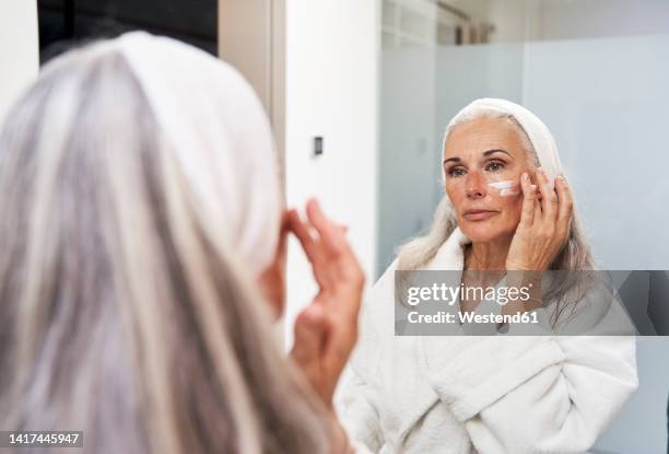 mature woman applying face cream in bathroom - crema facial fotografías e imágenes de stock