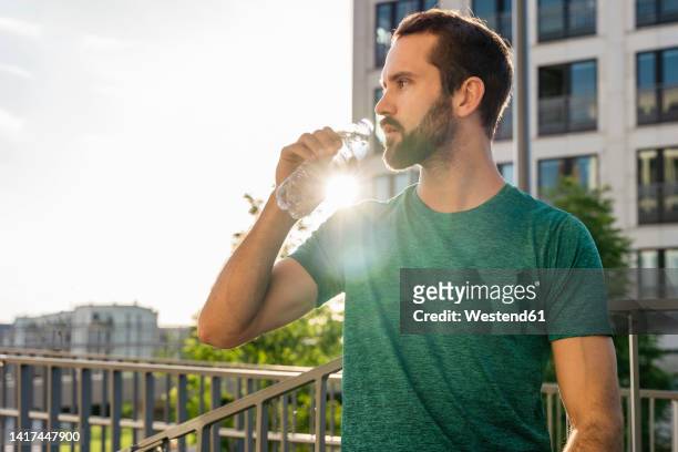 young man drinking water on sunny day - mann wasser trinken sport stock-fotos und bilder