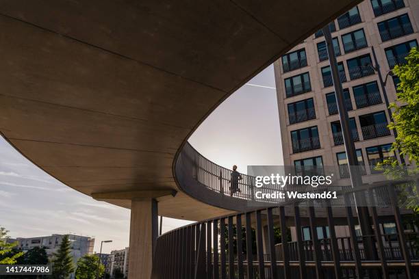 man running on elevated walkway in front of building - fußgängerbrücke stock-fotos und bilder