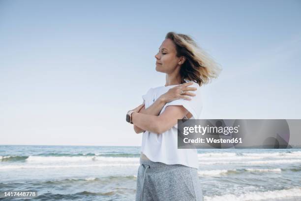 happy woman hugging self in front of sea - hugging self stock-fotos und bilder