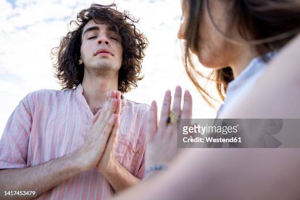 young couple meditating with hands clasped - couple praying stock pictures, royalty-free photos & images