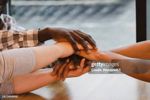 multiracial friends stacking hands at table in cafe - igualdad racial fotografías e imágenes de stock