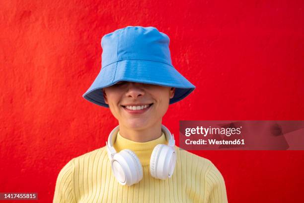 smiling woman with headphones and blue bucket hat in front of red wall - bucket hat stock pictures, royalty-free photos & images