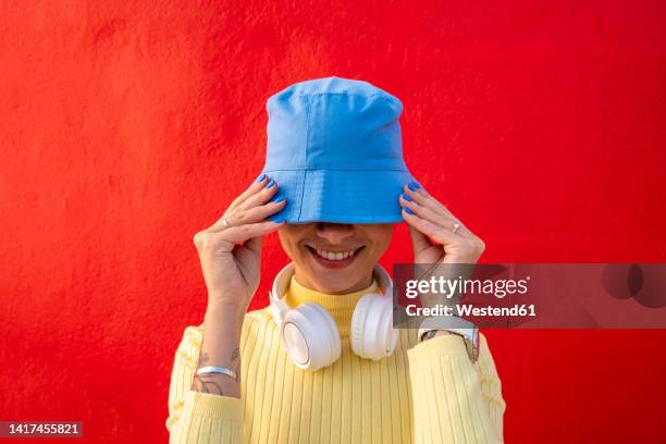smiling woman with headphones covering face with blue bucket hat - gorro bob fotografías e imágenes de stock
