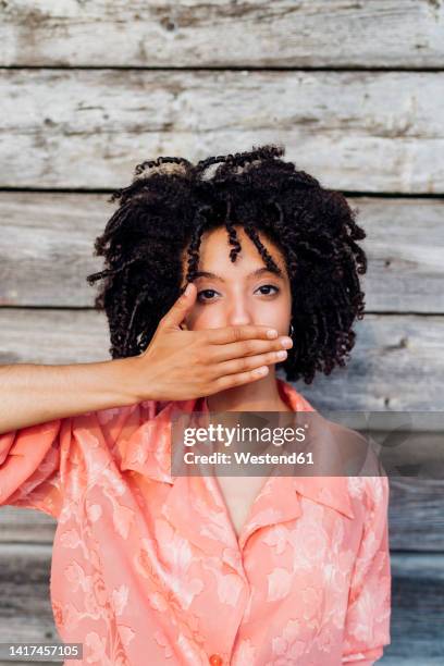 young woman covering mouth with hand in front of wooden wall - 3 wise monkeys stock pictures, royalty-free photos & images