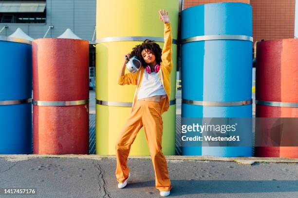 young woman carrying boom box on shoulder dancing in front of colorful pipes - ラジカセ ストックフォトと画像