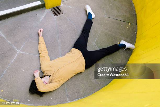 man covering eyes with hand lying unconsciously on floor by yellow wall - fainted stock-fotos und bilder