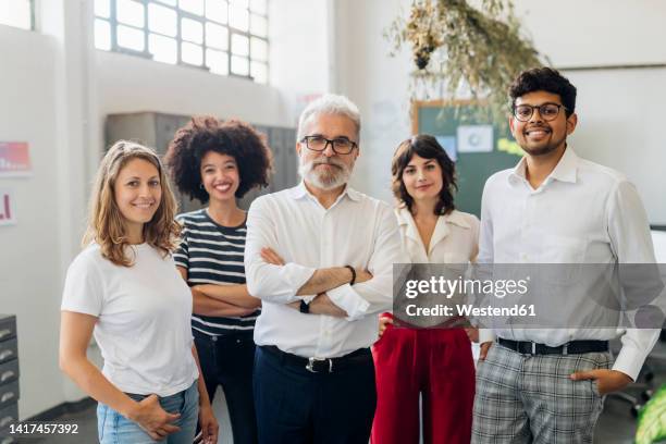 smiling multiracial colleagues standing together in office - organized group photo - fotografias e filmes do acervo