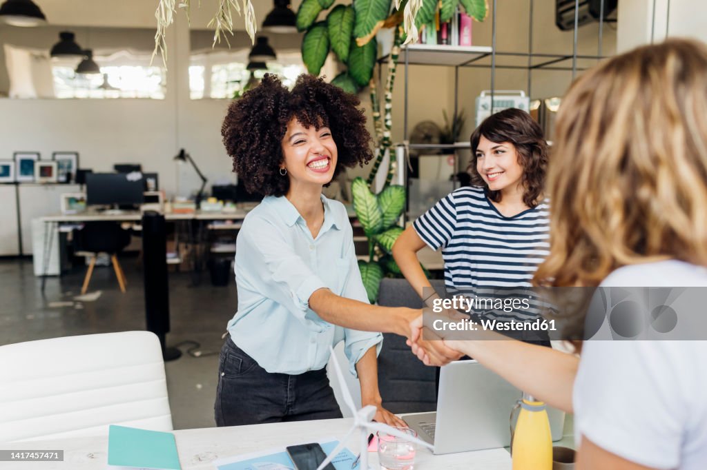 Happy businesswoman shaking hand with colleague at work place