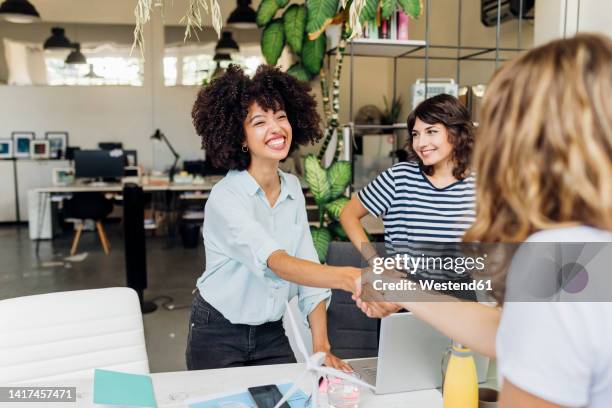 happy businesswoman shaking hand with colleague at work place - handshake photos et images de collection