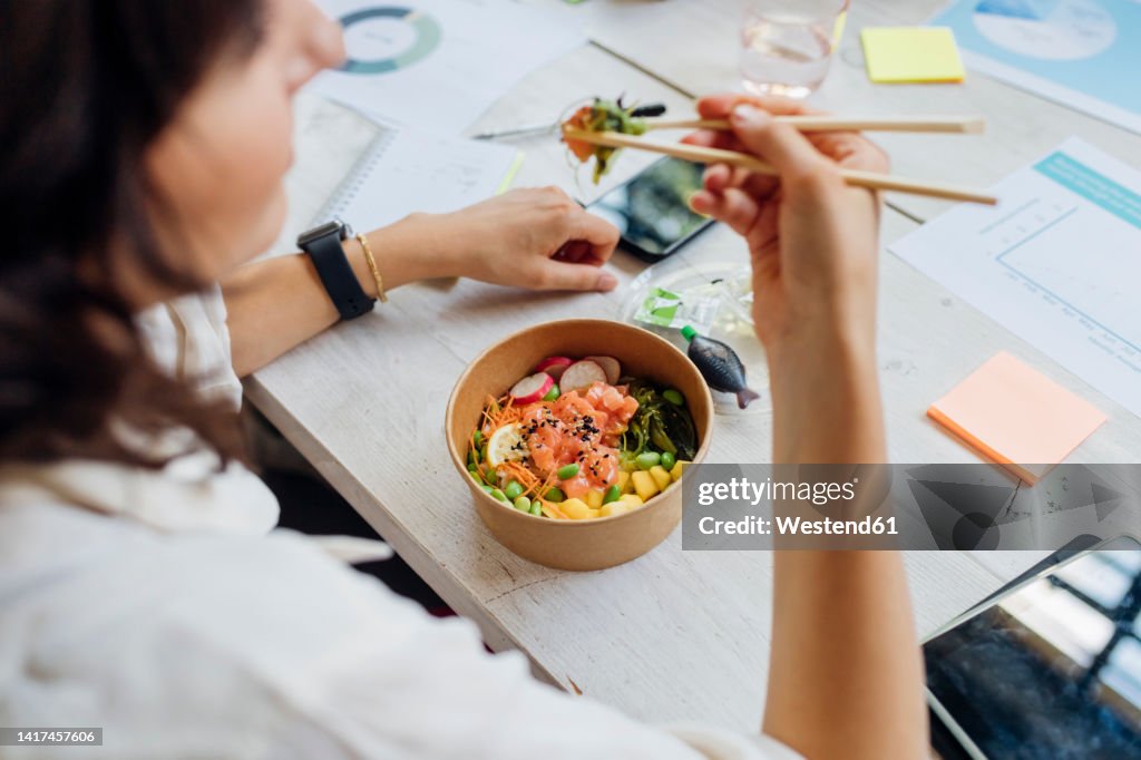 Businesswoman eating healthy poke bowl with chopsticks in lunch break at office
