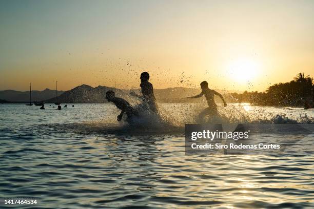 happy boys running to the sea on a beautiful sunset - happy people running stockfoto's en -beelden