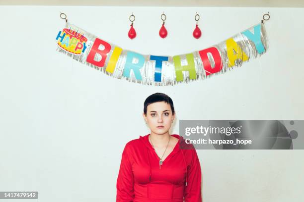 teenage girl with blank stare standing under a 'happy birthday' banner. - good; times bad times stock pictures, royalty-free photos & images