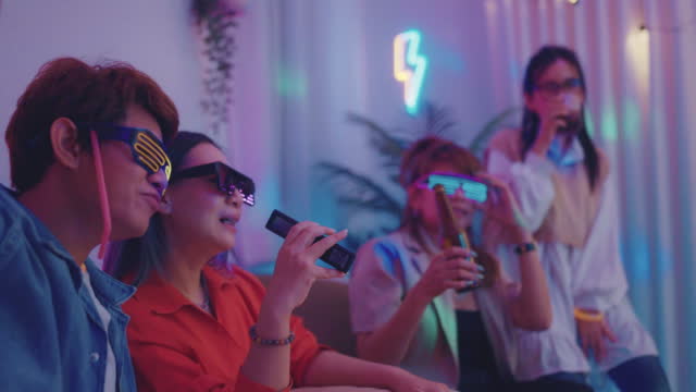 Group of happy asian young friends having fun karaoke and drinking beer in living room.