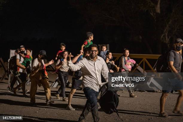 Immigrants walk along the U.S.-Mexico border barrier on their way to await processing by the U.S. Border Patrol after crossing from Mexico on August...