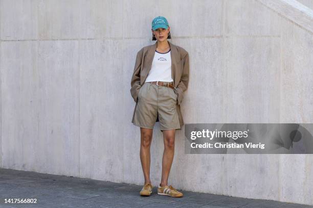 Model Vera van Erp wears brown Blazer: Envelope 1976, Tank top: A Modern Object, beige Shorts: Vintage, Shoes: Adidas, Cap: A Modern Object during a...