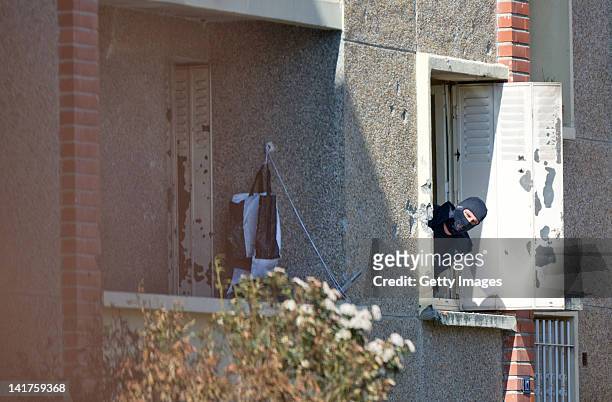 Hooded policeman looks outside the apartment as he investigates in the flat where Mohammed Merah, the man suspected of killing seven victims...