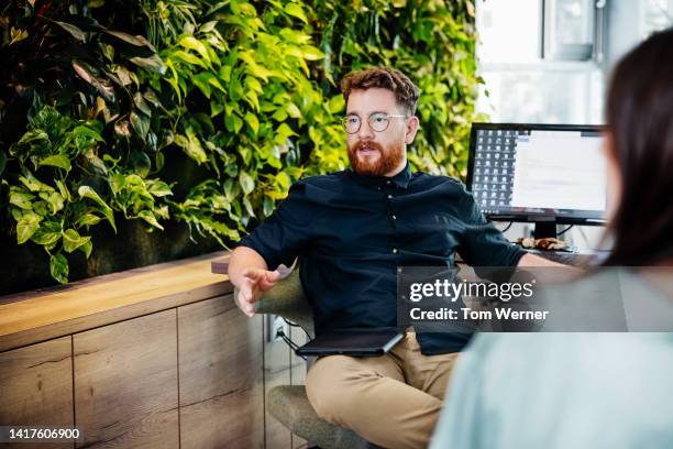 office employee sitting at desk in front of large display of plants - brightly lit office stock pictures, royalty-free photos & images