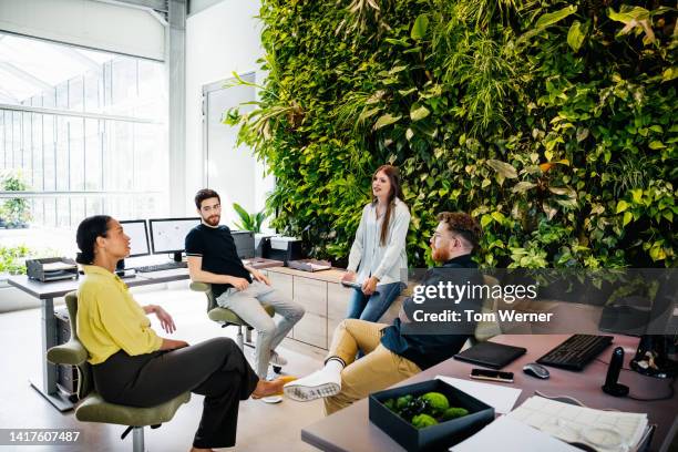 office colleagues having meeting in front of large plant display - men and women in a large group listening stock-fotos und bilder