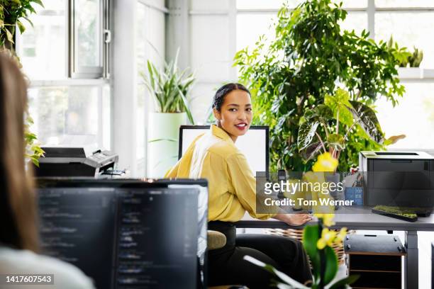 woman turning head while sitting at computer desk - looking over shoulder photos et images de collection