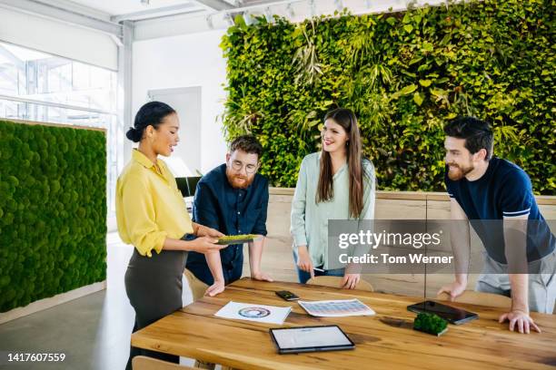 office team having meeting at large desk in their office - empresa de carácter social fotografías e imágenes de stock
