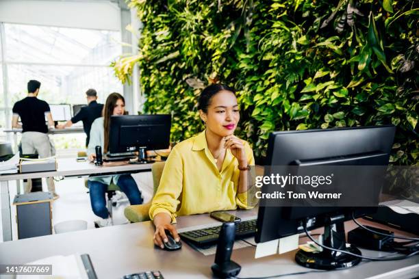 woman working in busy green office space with lots of plants - man made age stock pictures, royalty-free photos & images