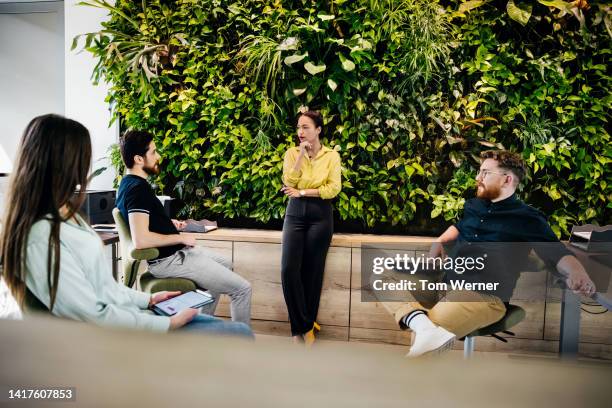 office meeting in front of large , leafy display - men and women in a large group listening stock-fotos und bilder