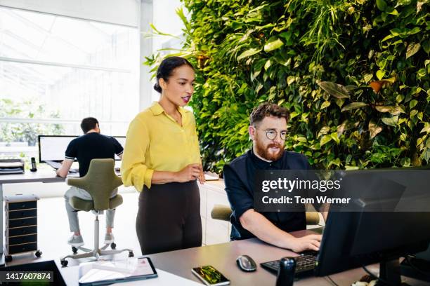 office manager talking to colleague about computer task - green blouse stock pictures, royalty-free photos & images