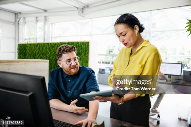 office manager showing documents on digital tablet to colleague - coworker foto e immagini stock