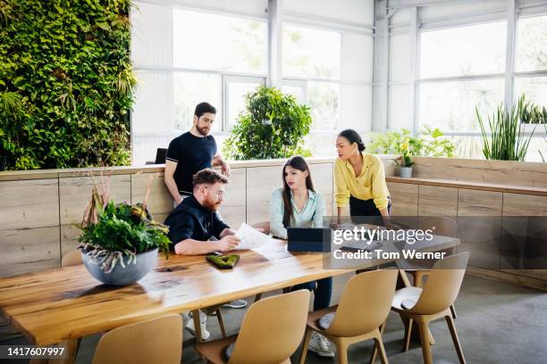 group of people gathered around desk for business meeting - empresa de carácter social fotografías e imágenes de stock
