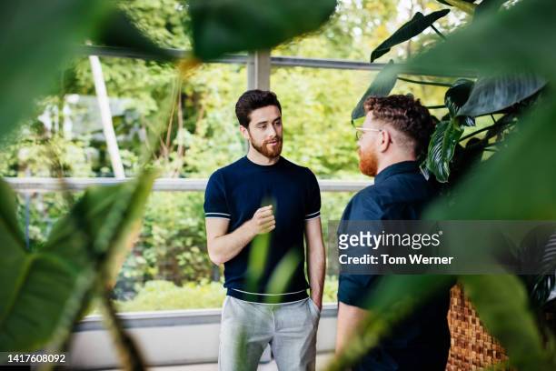 two colleagues talking amongst plants in green office - sustainable lifestyle stock pictures, royalty-free photos & images