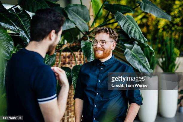 two colleagues standing amongst potted plants in green office space, talking - beautiful people talking stock pictures, royalty-free photos & images