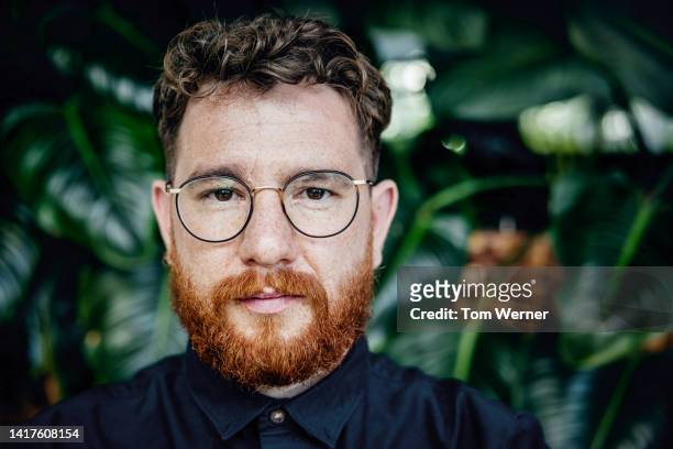 close up portrait of man with beard and glasses in front of foliage - kopfbild stock-fotos und bilder