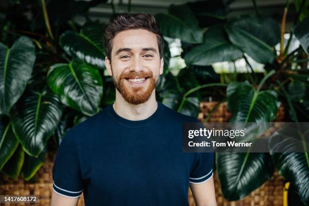 portrait of office employee standing in front of lush foliage - business man portrait smiling stock-fotos und bilder